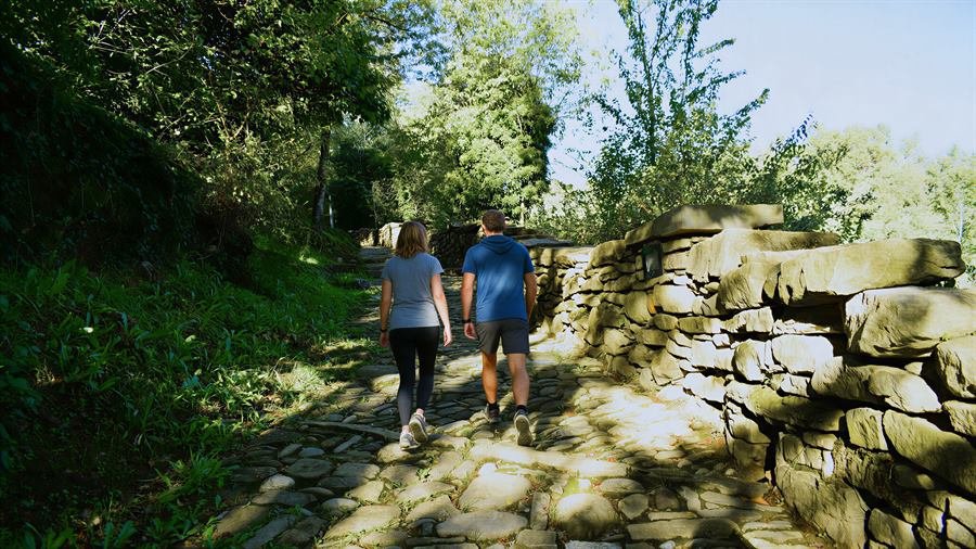 Dos paseantes por el camino empedrado de Casa Santiago, entre muros de piedra
