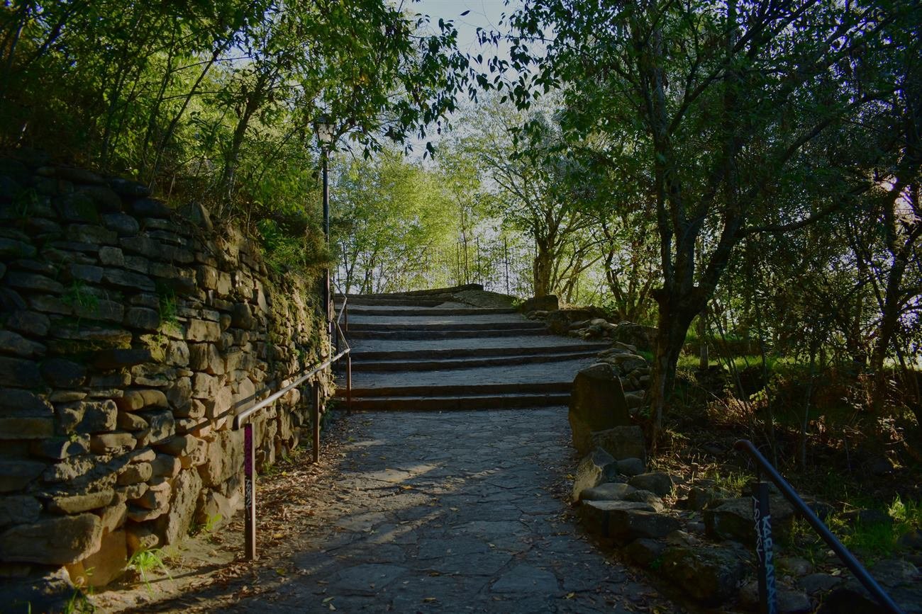 Escaleras de piedra con barandilla entre un muro de piedra y árboles, en la subida al casco antiguo de Aínsa